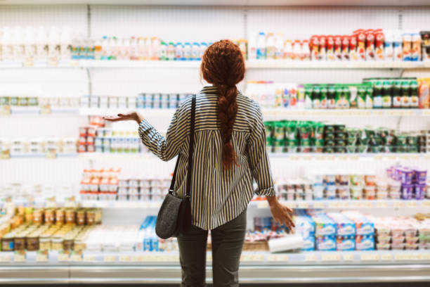 mujer joven con camisa a rayas desde atrás tratando de elegir productos lácteos en un supermercado moderno - beauty beautiful braids dairy product fotografías e imágenes de stock