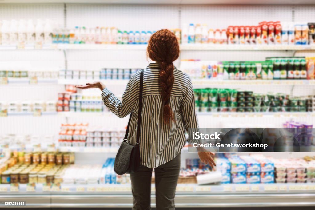 Young woman in striped shirt from back trying choose dairy products in modern supermarket Supermarket Stock Photo