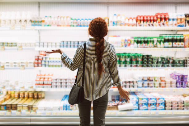 young woman in striped shirt from back trying choose dairy products in modern supermarket - department store shopping mall store inside of imagens e fotografias de stock