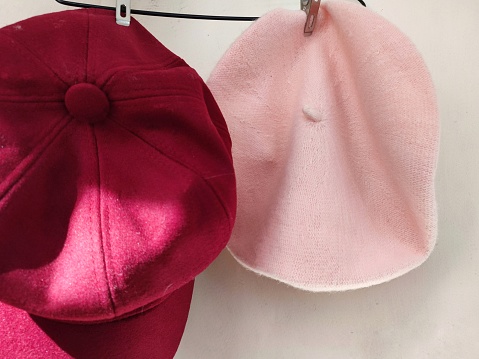 In selective focus of pink red hats hanging from a cloth hanger and sun drying ,white wall background