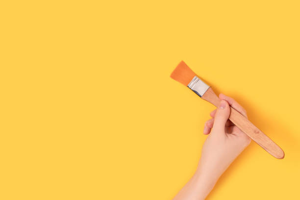 istock Female hand hold paintbrush on a yellow background. 1357297971