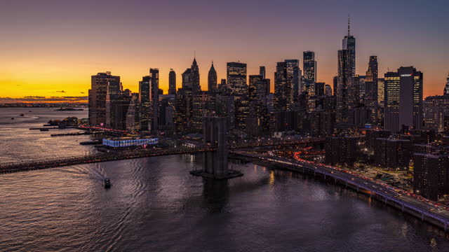 Evening hyperlapse of big modern city. Fly over bridges and view tall downtown skyscrapers against dimming sunset sky. Brooklyn Bridge in Manhattan, New York City, USA