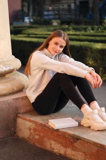 istock Young pretty stylish student girl in cozy sweater happily looking in camera during study break outdoor 1357302021
