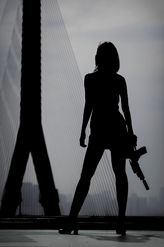 Silhouette of a woman holding a gun with a cloudy sky in the background.