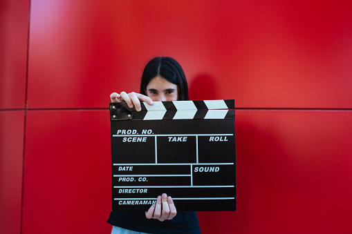 A young girl holding a movie clapboard in front of a red background. Movie film director concept.