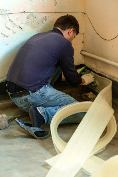 istock The man glues a damping tape on a wall bottom, protection for a floor coupler. 1357309321