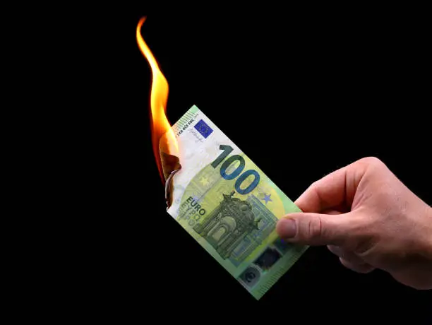 Photo of male hand holds a burning 100 euro banknote isolated on black background, concept image of inflation