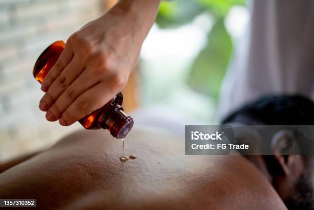 Hands of a massage therapist applying oil on a man's back at a spa