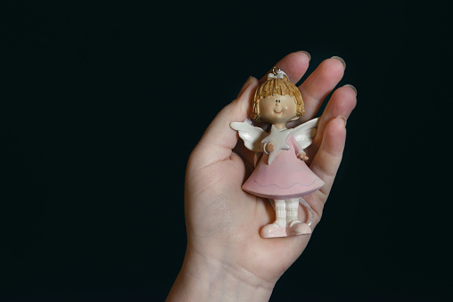 figure of a cute Christmas angel on a dark background in the hands of a girl. copy space. christmas and new year celebration concept. New Year's wishes. miracles on the bright holiday of Christmas