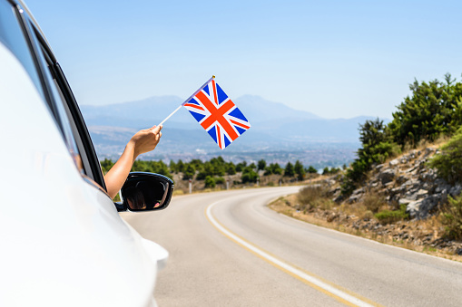 Woman holding United Kingdom flag from the open car window driving along the serpentine road in the mountains. Concept