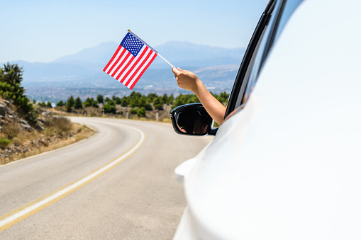 Woman holding USA flag from the open car window driving along the serpentine road in the mountains. Concept