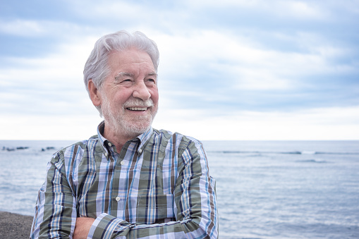 Portrait of old senior man smiling enjoying sea holiday or retirement. Cloudy sky and horizon over water