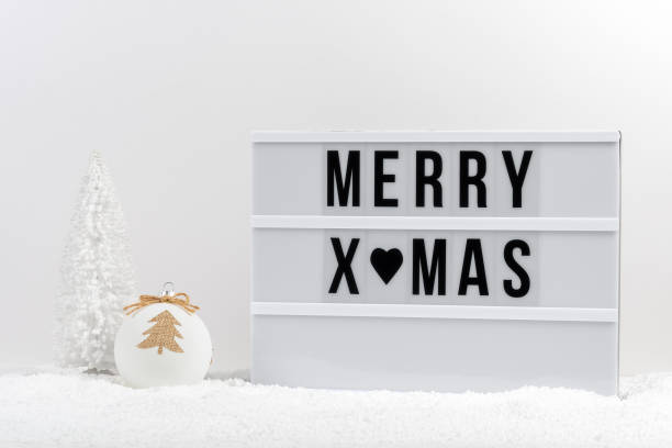 istock White Christmas tree, Christmas bauble and lightbox with text MERRY XMAS on a table with snow. Minimal Christmas or New Year concept. 1357316131