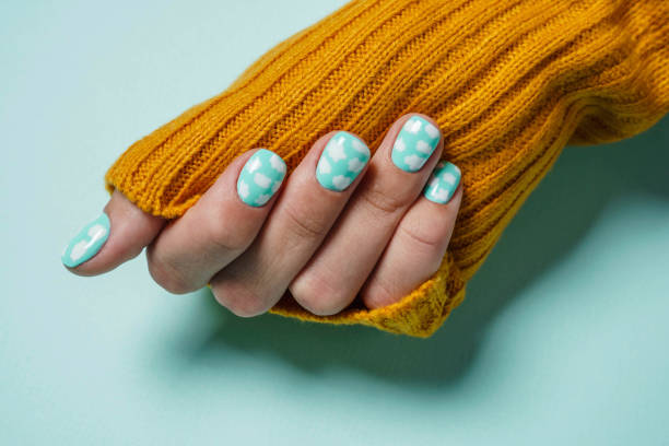 Beautiful female fingers with colored manicure with clouds, the sleeve of a warm wool sweater mustard color stock photo