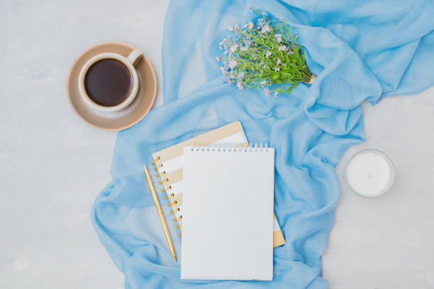 istock Flat lay composition with mockup notebook, cup of coffee and small blue flowers on a light background 1357322471