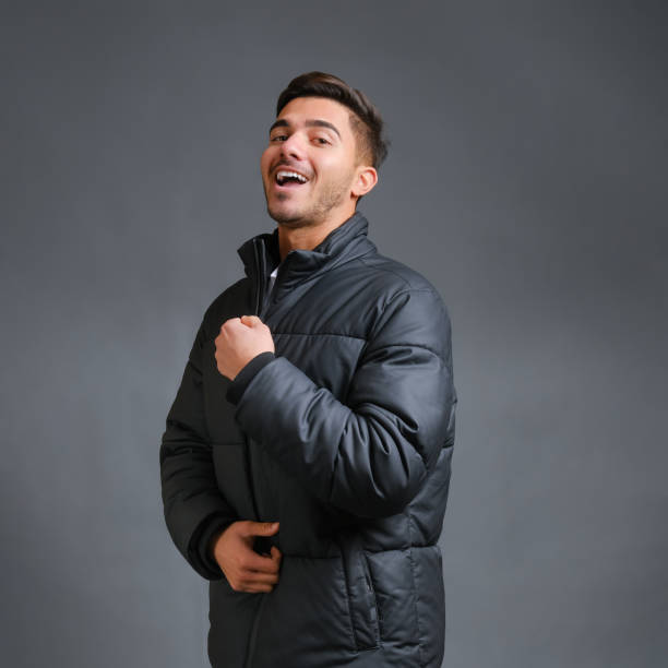 Man on a gray background is warmly dressed in a black down jacket Smiling stylish guy model on a gray background is warmly dressed in a black down jacket. High quality photo Jacket stock pictures, royalty-free photos & images