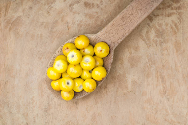 Spoon of nances on a wooden table Byrsonima crassifolia fruits are known as nance, nanche, changunga and other common names in tropical America. The little oily fruits are eaten raw or used as ingredients to prepare desserts peach color table stock pictures, royalty-free photos & images