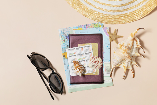 Minimal summer travel vacation concept. Passport with map, passport, starfish, glasses, bank card on sand color background. Flat lay.