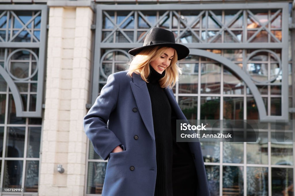Lifestyle portrait of fashionable woman wearing winter or spring outfit, felt hat, gray wool coat and turtleneck. Outdoors. Female stylish Model smiling, walking city Street. Street fashion trend Lifestyle portrait of fashionable woman wearing winter or spring outfit, felt hat, gray wool coat, turtleneck. Outdoors. Female stylish Model smiling, walking city Street. Street fashion trend Fashion Stock Photo