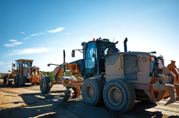 Construction and leveling of the ground during road construction works by a grader Construction and leveling of the ground during road construction works by a grader, blue sky, back light road scraper stock pictures, royalty-free photos & images