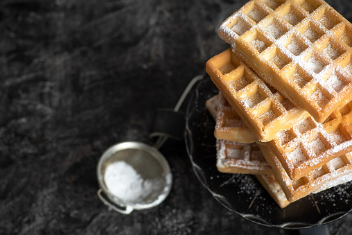 Belgian waffles on a pile on a black rustic background. Stock photo.