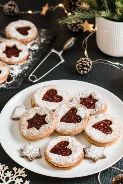 istock Ready Linzer cookies with berry jam on a plate and Christmas decorations on a dark background. Cooking Christmas treats. Lifestyle. Vertical view. Close-up 1357339395