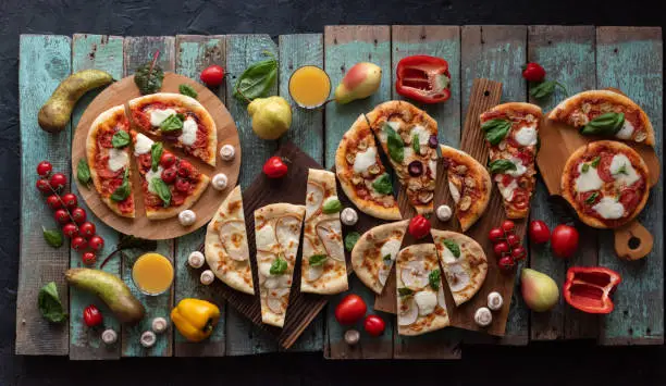 Six cutted pizzas with mushrooms, tomatoes, basil, pears on old painted wood background overhead view