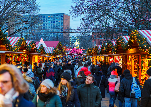 Berlin, Germany - December 29, 2019: Christmas Market at Gendarmenmarkt (Weihnachtszauber Gendarmenmarkt) at night in Berlin. Local people and tourists wander around the market stalls, shop and drink mulled wine.