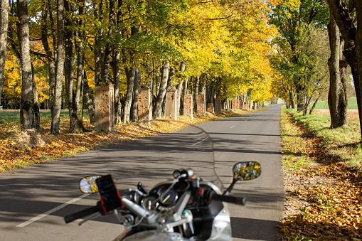 A first-person motorcycle journey. Autumn road leaves are yellow, green and orange. Selective focus. Moto dashboard. Motorcycle driver riding in forest landscape.