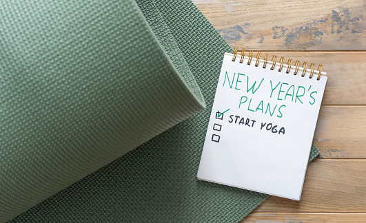 Notepad on the wooden background with the inscription - New year's plan - start yoga and green sports mat