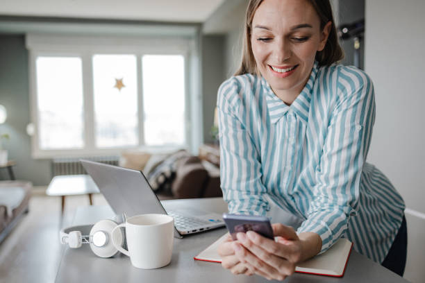 istock Blond hair woman using mobile phone at home and smiling 1357343616