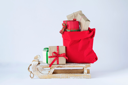 Santa Claus red bag full of christmas presents on wooden sleigh on light background stock image