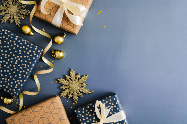 istock Christmas gifts with golden baubles, snowflakes and ribbon on dark blue background. Flat lay, top view, copy space. 1357347322