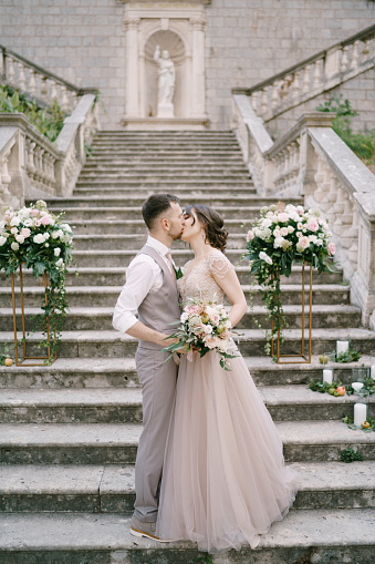 Groom kisses bride while standing on the stone steps near the old villa. High quality photo