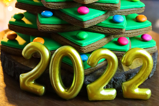 Stock photo showing close-up view of wooden chopping board containing a stack of star shaped gingerbread biscuits, decorated with green fondant icing and multi-coloured candy coated chocolate sweets, forming a Christmas tree. Home baking concept.