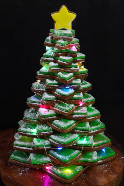 緑のフォンダンアイシングと積み重ねられたジンジャーブレッドスタークッキーのイメージクリスマスツリーは、照らされた妖精のライト、マルチカラーのキャンディコーティングチョコレ� - star shape christmas ornament heap stack ストックフォトと画像