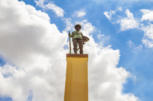 Goiânia, Goias, Brazil – December 04, 2021: Photo of the statue that is right in the middle of Praça do Bandeirante in Goiania. Bandeirante Square in Goiania. The monument to the bandeirante, symbol of the square, was inaugurated on November 9, 1942. The monument was created by the plastic artist Armando Zago in response to the request of the Academic Center XI de Agosto of the Faculty of Law of São Paulo, to be donated to the people Goiás. The bronze sculpture is three and a half meters high and portrays the pioneer Bartolomeu Bueno da Silva in full body, holding a baton in his hands and armed with a blunderbuss.