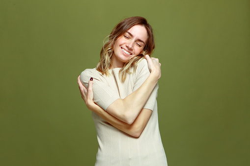 Happy relaxed young woman embrace herself smiling on green background. Self love, self-care, body positive