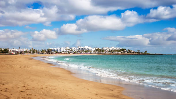 ランサローテ州プエルト・デル・カルメンのプラヤ・デ・ロス・ポシロスビーチの景色。ターコイズブルーの海水と砂浜のパノラマ, カナリア諸島の観光リゾートの白い家, スペイン - プエルトデルカルメン ストックフォトと画像