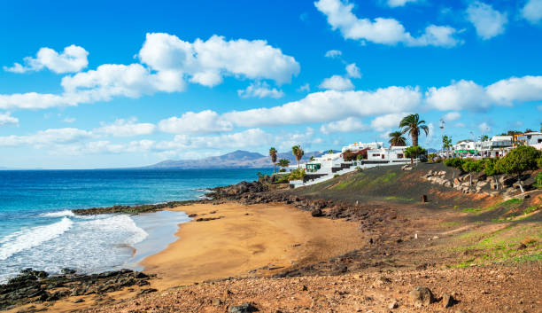 view of playa el barranquillo beach in puerto del carmen, lanzarote. sandy beach with turquoise ocean waves, white houses and mountains, canary islands, spain - lanzarote bay canary islands beach imagens e fotografias de stock