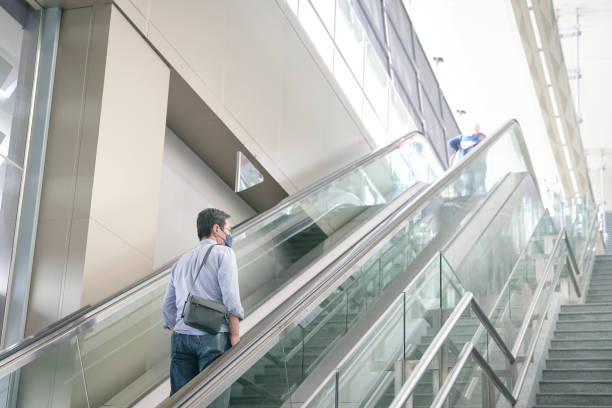 istock Man with face mask on using the escalator inside a modern building. 1357355058