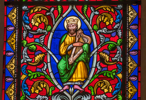 Vertical photo of the beautiful colourful stained glass window depicting Saint John the Evangelist, holding a golden goblet containing a purple dragon, with the Heraldic Eagle of St John at his feet, as seen from inside the heritage listed Saints Mary and Joseph Catholic Cathedral, Armidale, New England high country, northern NSW.