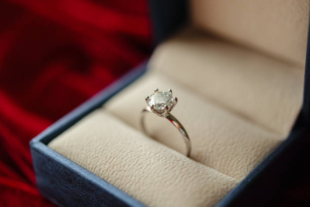 istock Diamond ring in jewelry gift box on red fabric background 1357364948