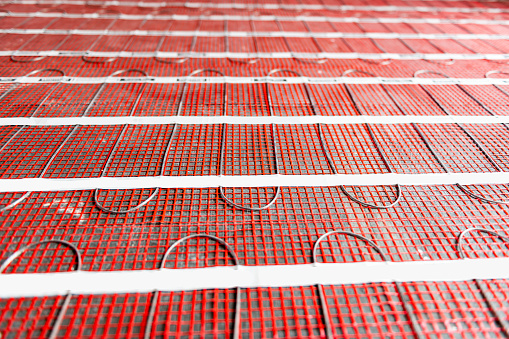 Process of instalation of electric underfloor heating mats on cement floor in new house. Radiant heating cable is attached to tough fiberglass mesh. Process of renovation, best way of making home warm