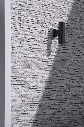 Sunlight and shadow on surface of outdoor black cylinder wall lamp on vintage white and gray ledgestone wall in vertical frame