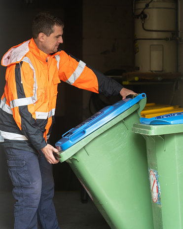 Garbage removal man picks up garbage bins from a building
