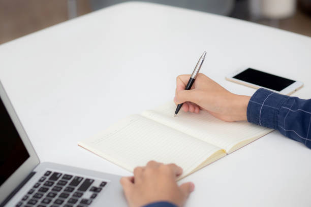 istock Closeup hand of business man writing on note while using laptop computer on desk at home, male planning on note for business success, author and blog, businessman working on table, employee and job. 1357390175