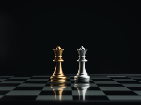 Piezas de ajedrez de reina dorada y plateada de pie juntas en un tablero de ajedrez sobre fondo oscuro. Concepto de líder, equipo, enemigo, cooperación, asociación y estrategia de negocio. photo