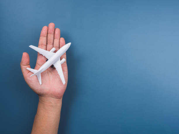 istock White plane toy model on hand on a blue background with copy space, top view, minimal style. White airplane, flat lay design. Flight, travel concept. 1357393973