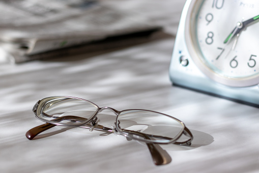 Eyeglasses, table clock and newspaper on a desk by the window